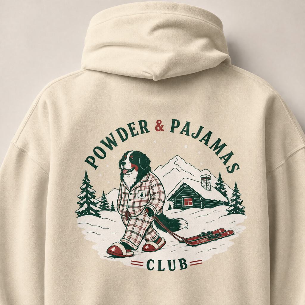 Close up of the back of a sand colored hoodie with a dog design and "POWDER & PAJAMAS CLUB" text.