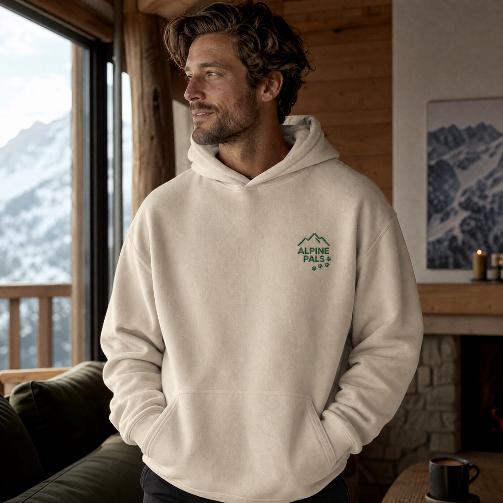Man wearing a sand colored hoodie with a logo, standing in a cozy room with a mountain view.