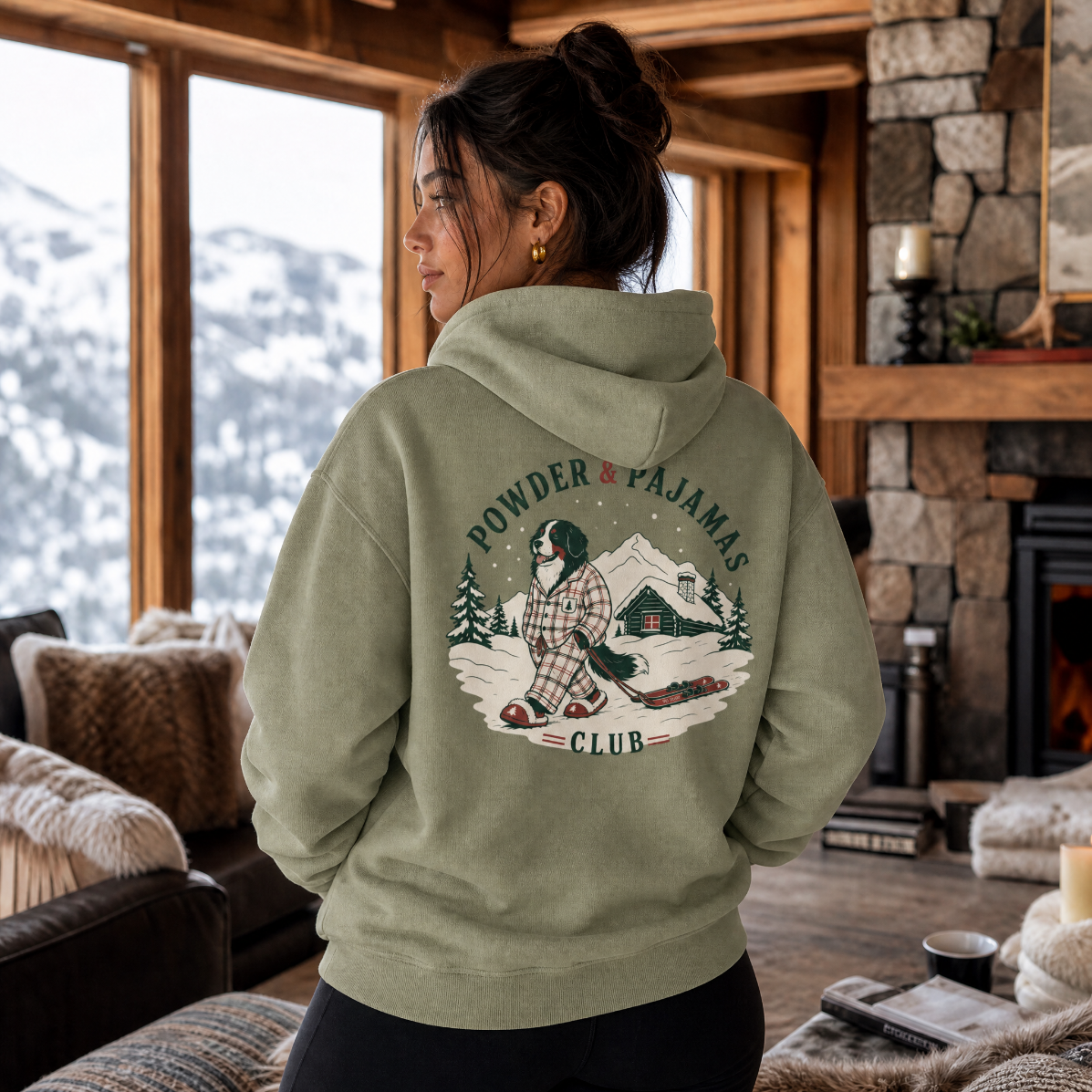 Woman wearing a hoodie with 'Powder Pajamas Club' design in a cozy living room.