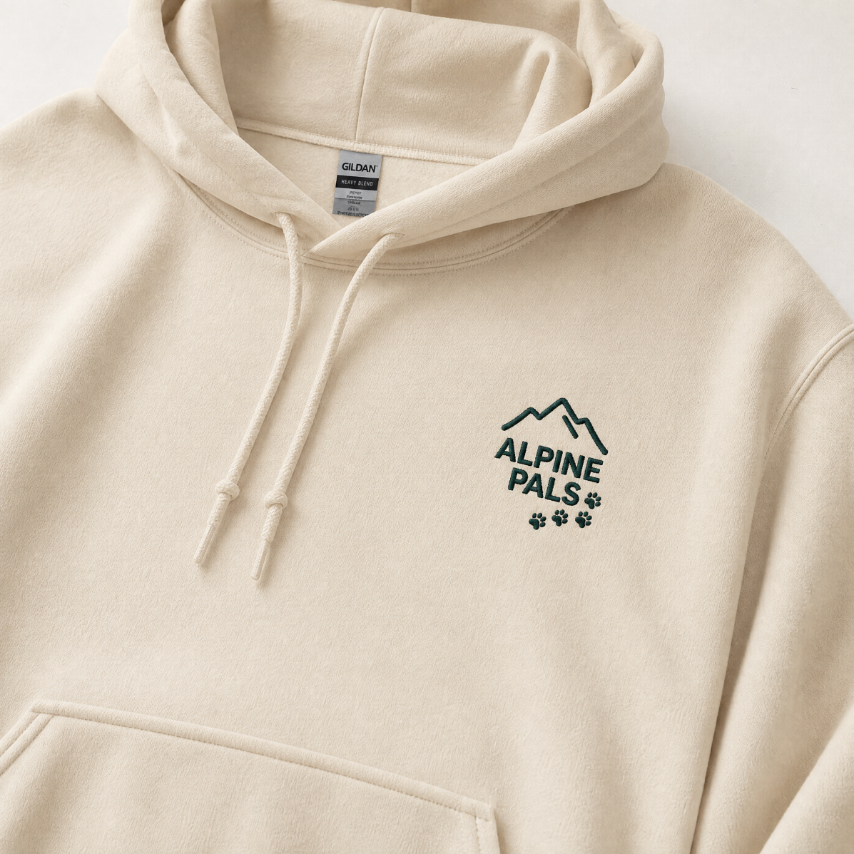 Close up of a sand colored hoodie with 'Alpine Pals' logo.