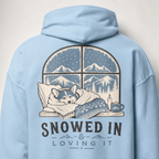 Light blue hoodie with a graphic of a dog by a window and 'Snowed In & Loving It' text on the back.