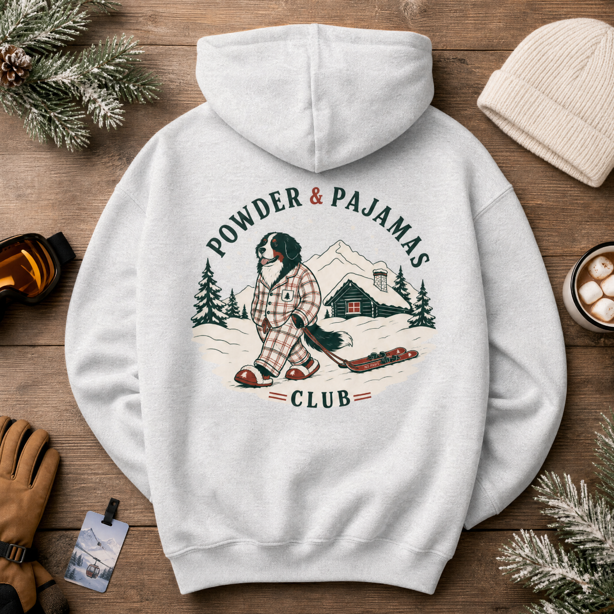Ash gray hoodie with 'Powder & Pajamas Club' design on a wooden surface with winter accessories.