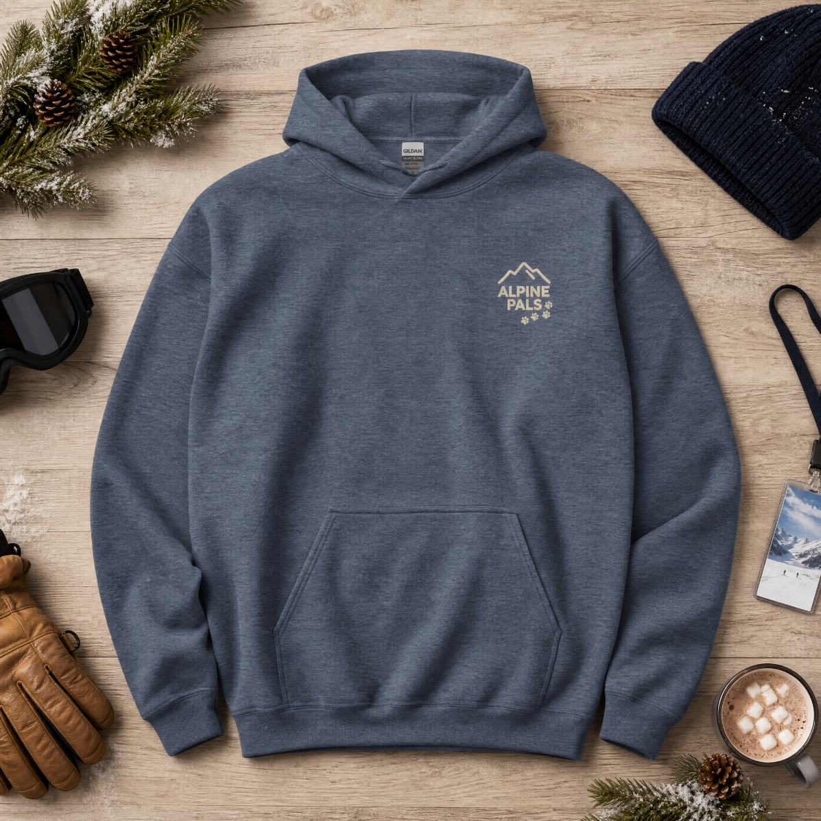 Heather sport dark navy hoodie with 'Alpine Pals' logo on a wooden surface with winter accessories.