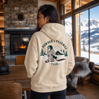 Woman wearing a sand colored hoodie that has a dog print with "POWDER & PAJAMAS CLUB" text.