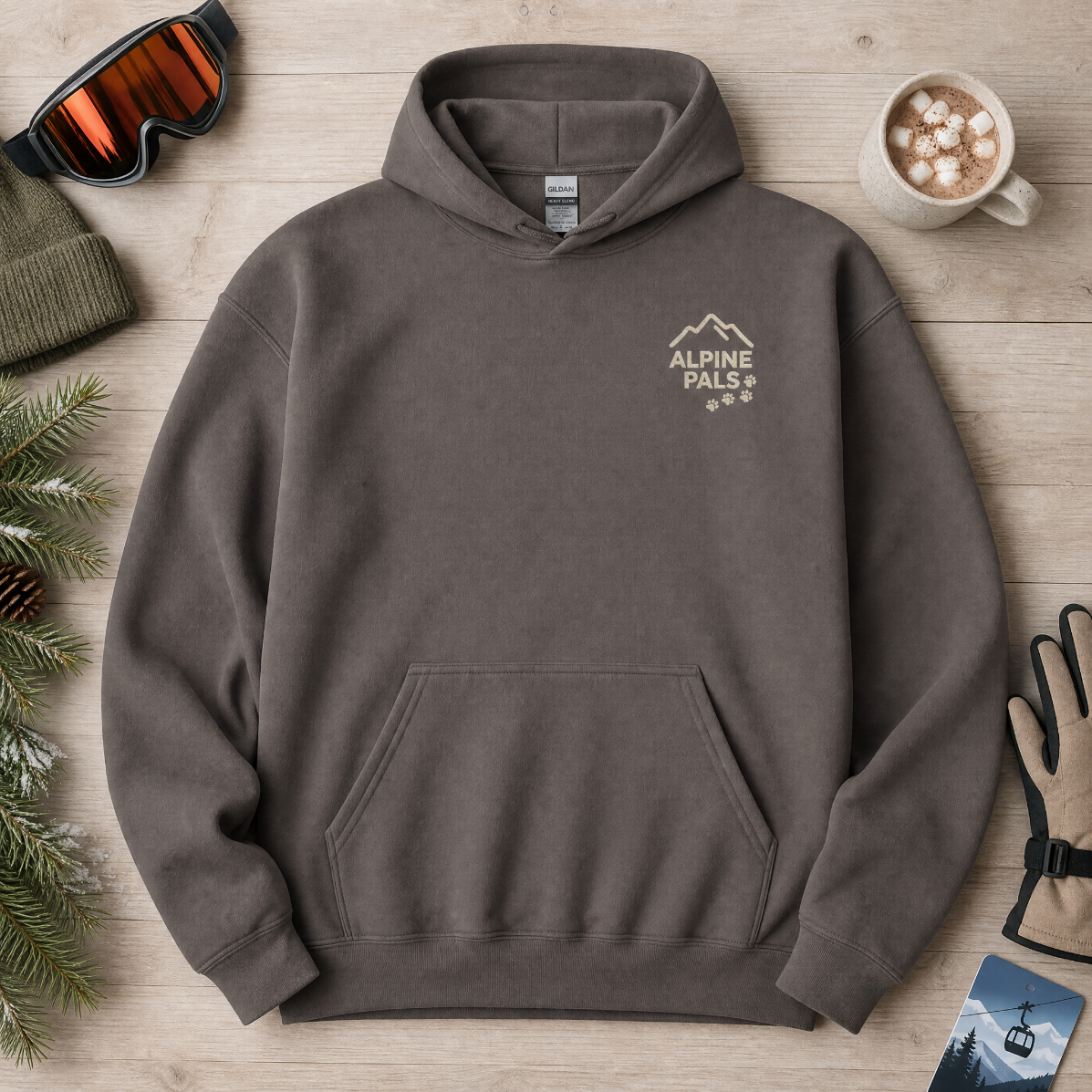 Charcoal gray hoodie with 'Alpine Pals' logo on a wooden surface with winter accessories.