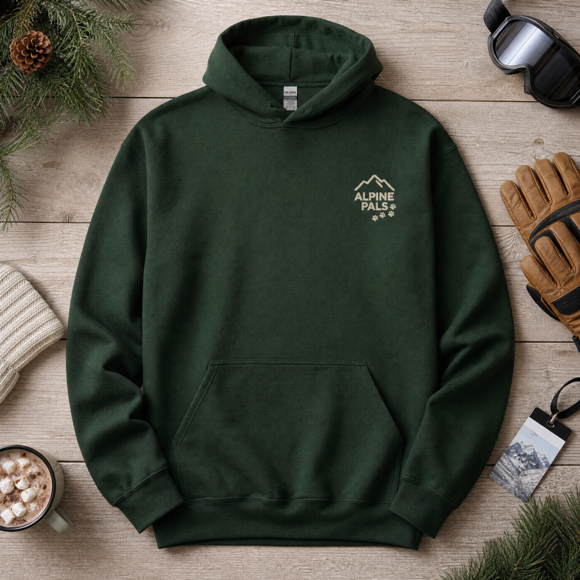Forest green hoodie with 'Alpine Pale' logo on a wooden surface with winter accessories.