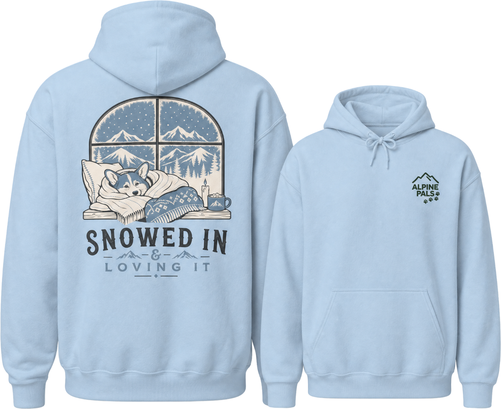 Light blue hoodie with a graphic of a dog by a window and 'Snowed In & Loving It' text on the back, with 'Alpine Pals' logo on the front.