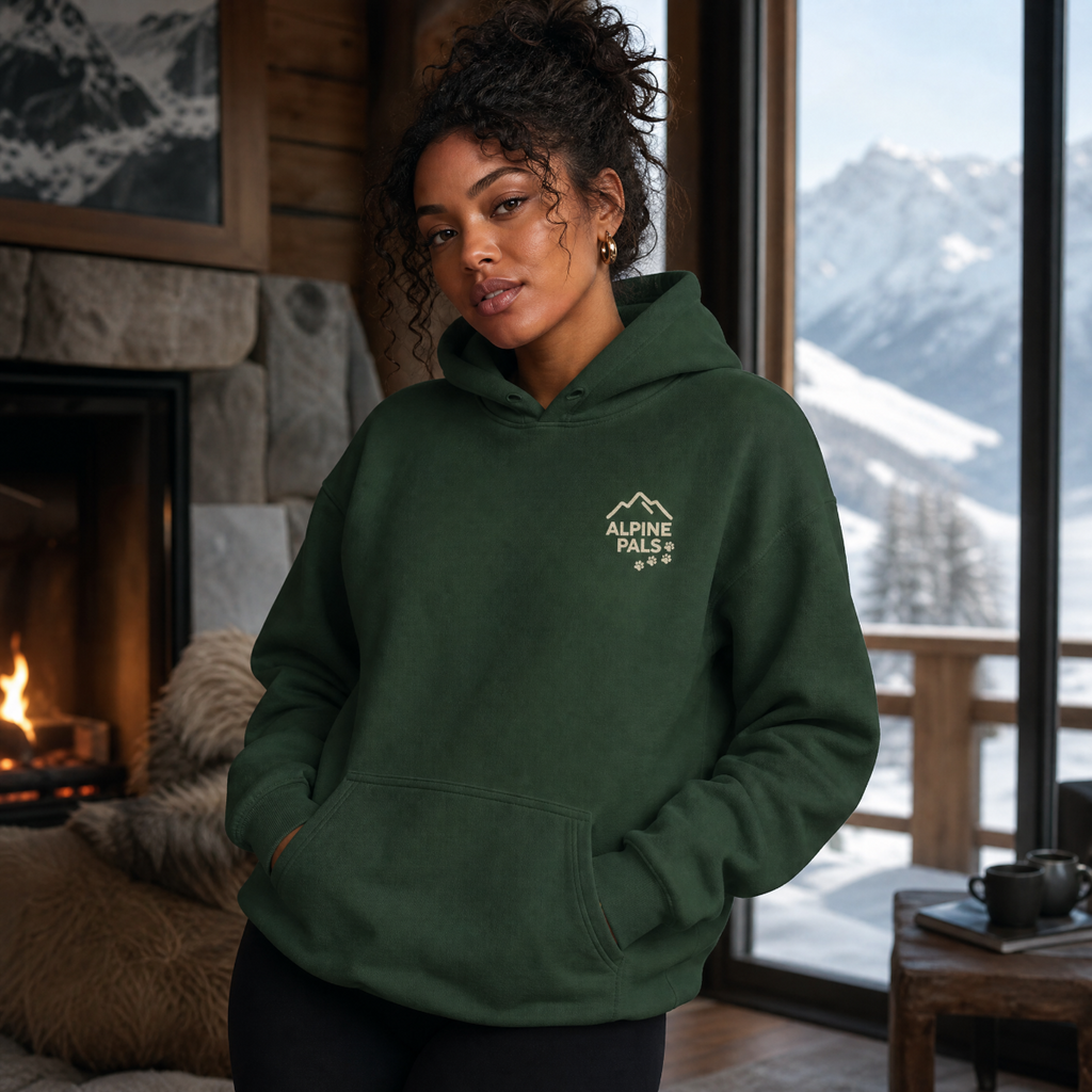 Woman wearing a forest green hoodie with a logo in a room with a fireplace and mountain view.