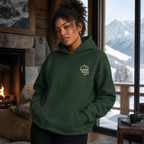 Woman wearing a forest green hoodie with a logo in a room with a fireplace and mountain view.