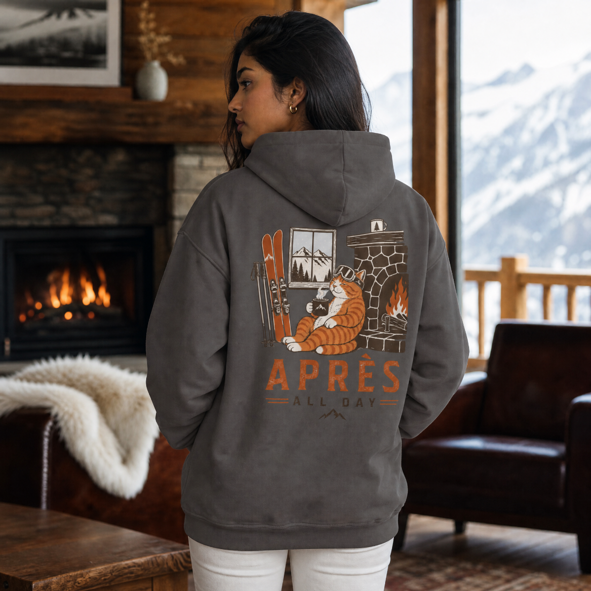 Person wearing a hoodie with a graphic design and 'APRES ALL DAY' text in a cozy indoor setting.