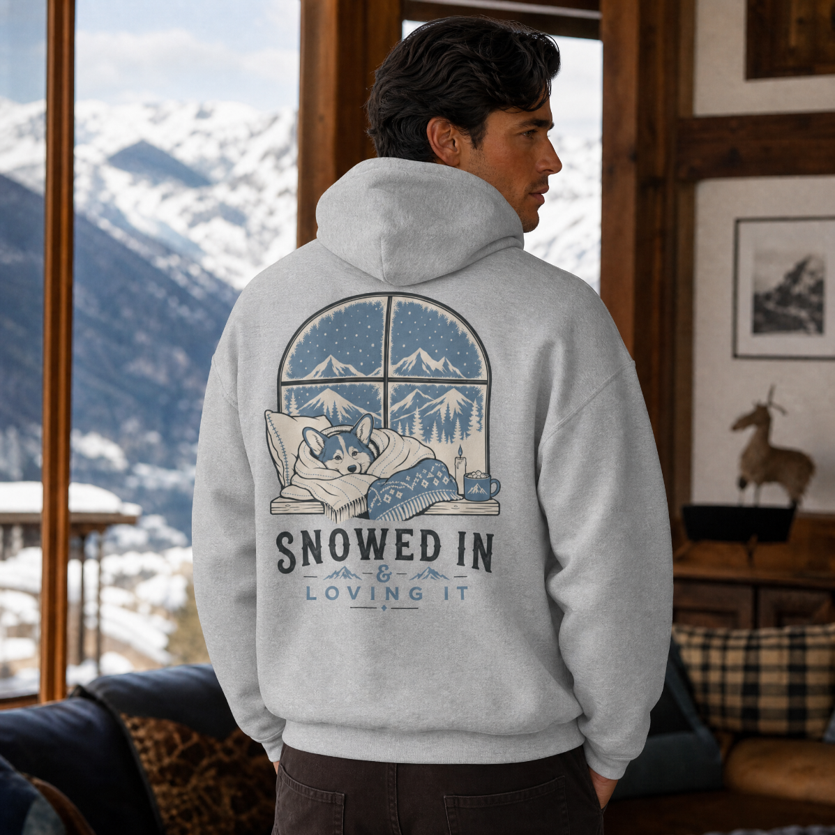 Man wearing a sport grey hoodie with a corgi design in a cozy lodge.