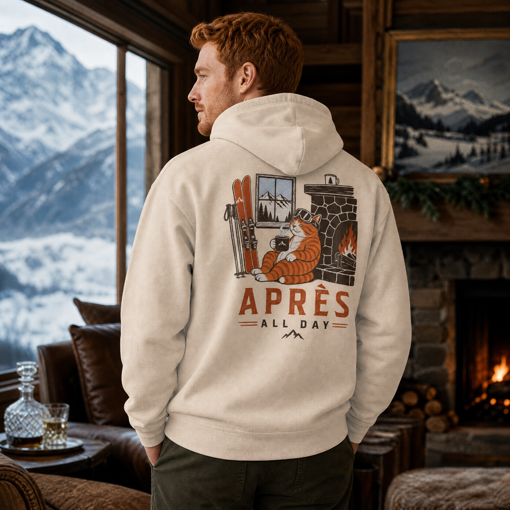 Man wearing a hoodie with a mountain and cabin design, standing in a cozy room with a fireplace and mountain view.