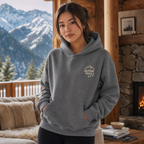 Woman wearing a graphite gray hoodie with 'Alpine Pals' logo in a cozy living room with mountain view.