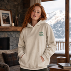 Woman wearing a sand colored hoodie with a logo in a cozy living room with a mountain view.