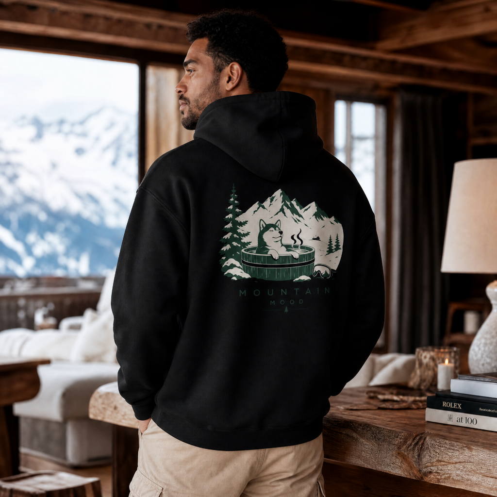 Man wearing a black hoodie with a mountain graphic in a cozy room with mountain views.