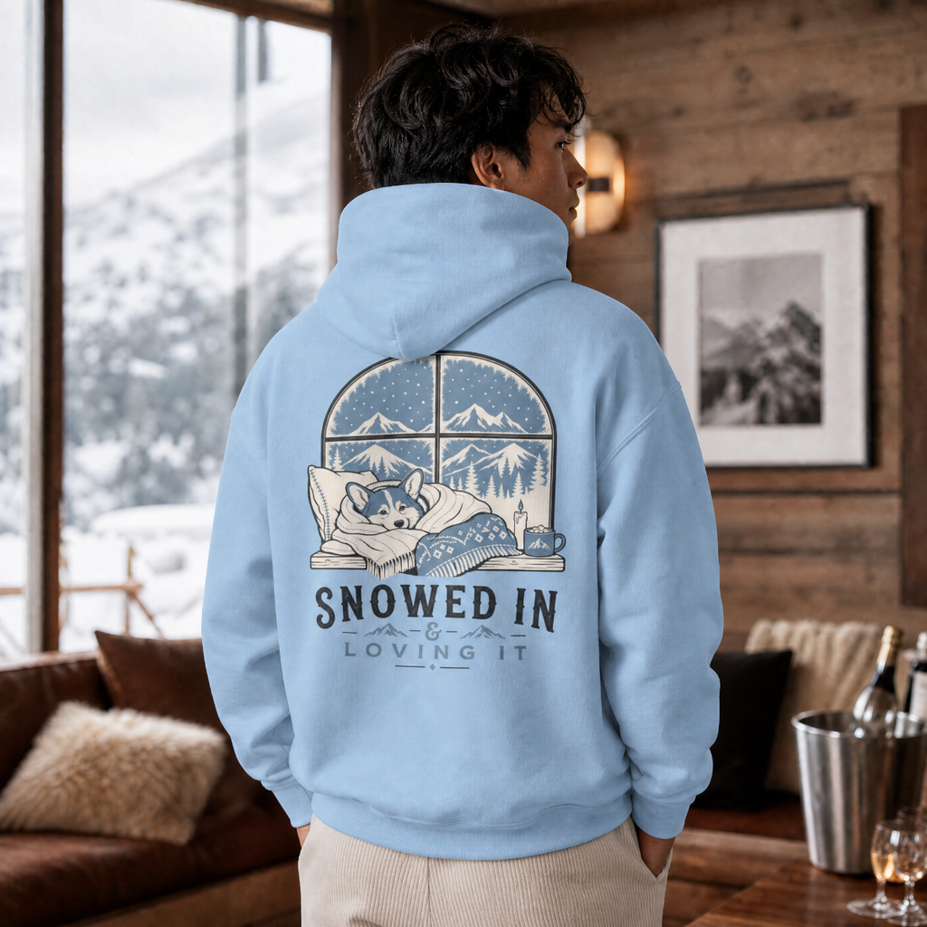 Person wearing a light blue hoodie with a graphic design and text, standing in a cozy room with a snowy view outside.