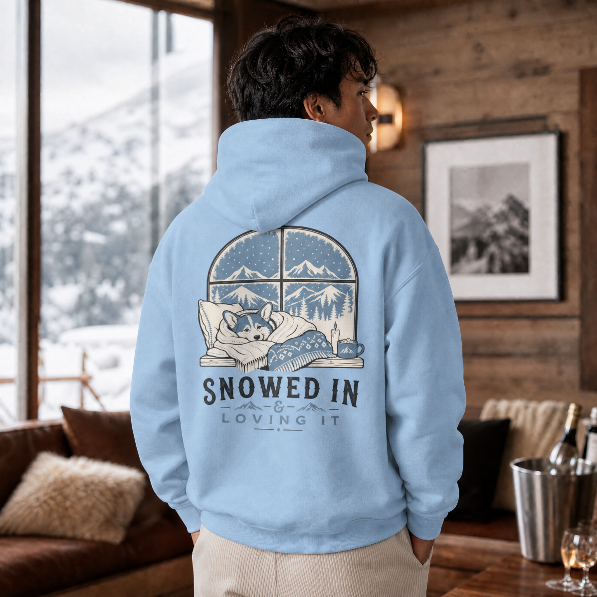 Person wearing a light blue hoodie with a graphic design and text, standing in a cozy room with a snowy view outside.