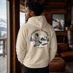Man in a cozy chalet setting wearing a sand colored hoodie that has a dog print design with 'POWDER & PAJAMAS CLUB' text.