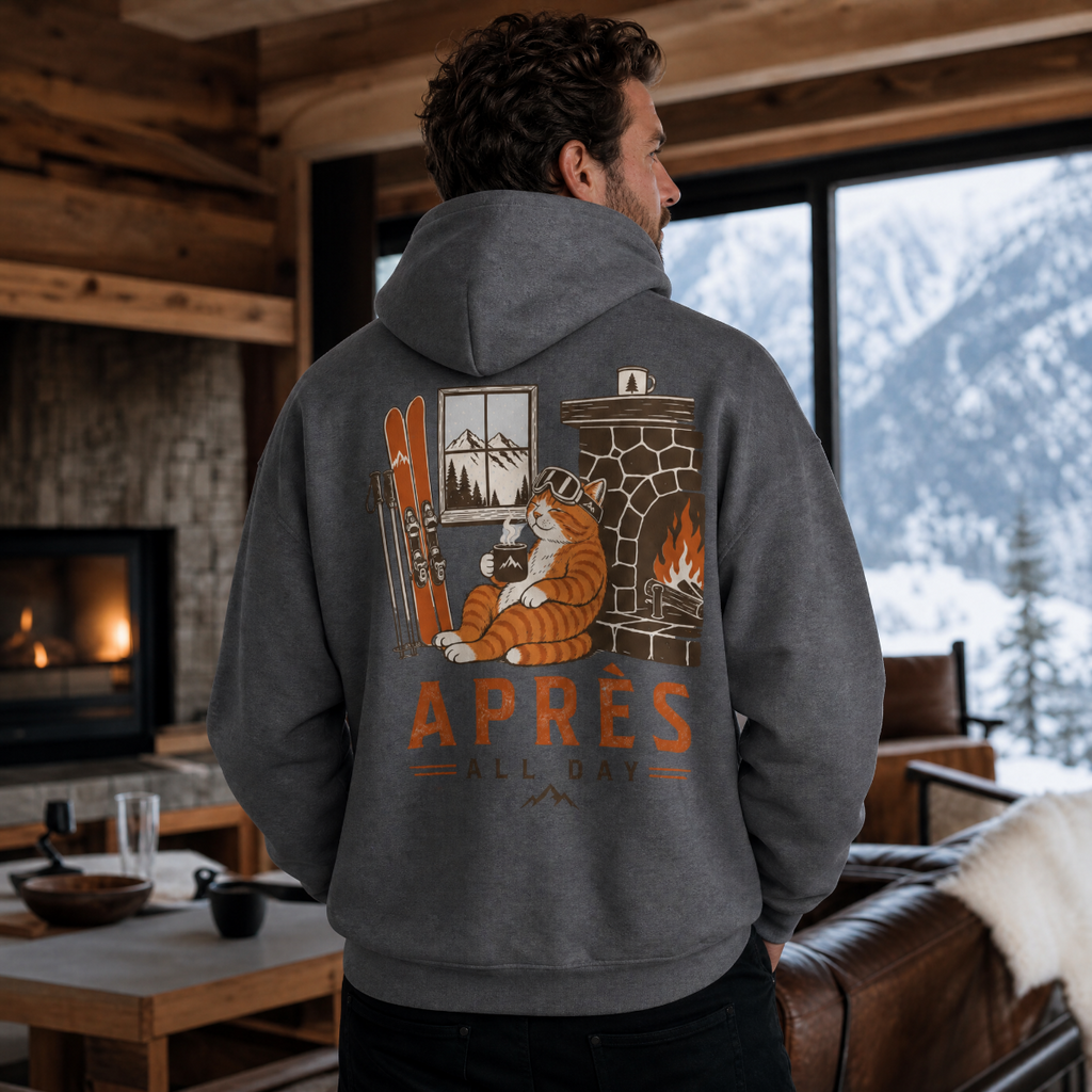 Man wearing a hoodie with a cat and fireplace design, standing in a cozy room with a mountain view.