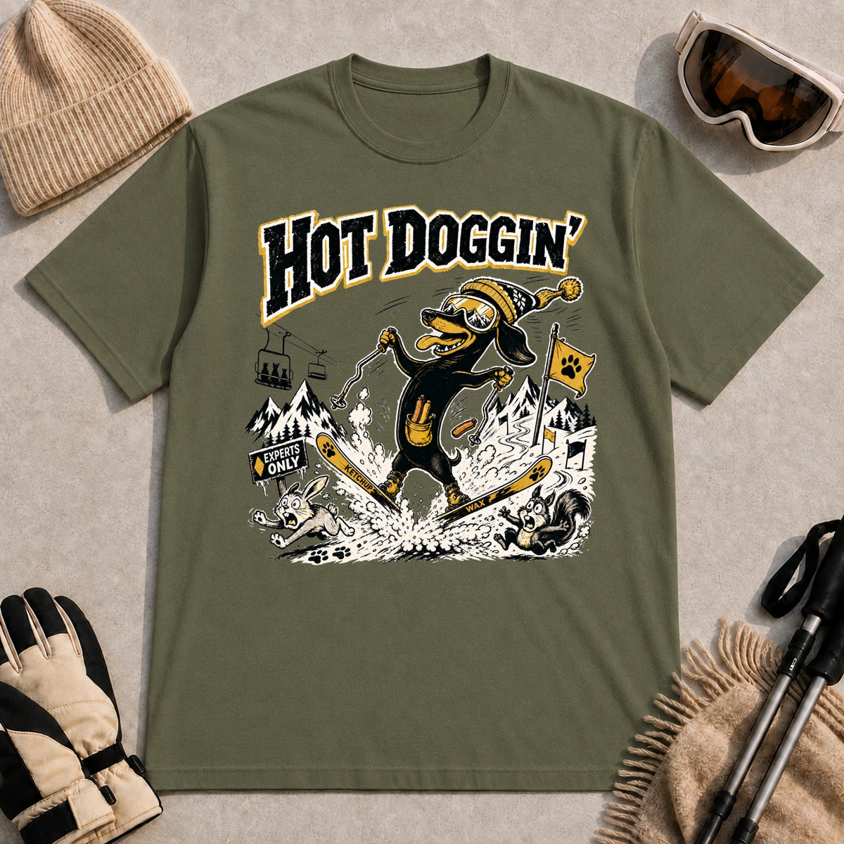 Military Green tee featuring a goggle-wearing dog skiing in a spread-eagle pose while startling woodland animals, with the phrase “Hot Doggin’.”