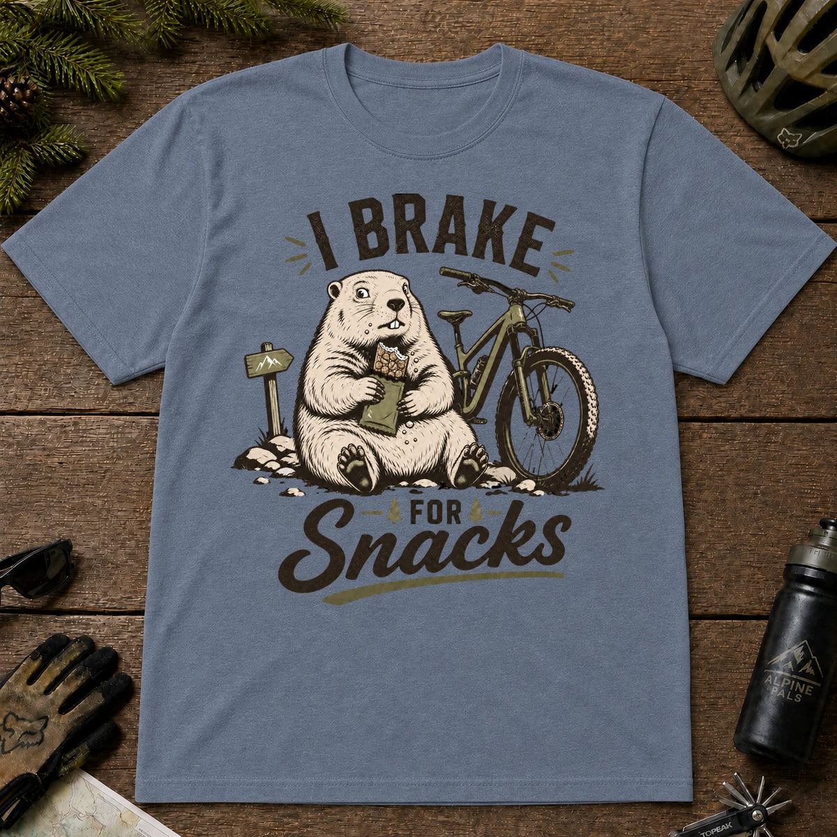 Heather Indigo tee featuring a snack-loving groundhog sitting beside a mountain bike and holding a bag of snacks, with the phrase “I Brake for Snacks.”