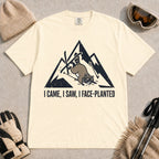 Ivory tee featuring a raccoon face-planting into the snow beneath a distressed mountain graphic with the phrase “I Came, I Saw, I Face-Planted.”
