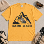 Mustard tee featuring a raccoon face-planting into the snow beneath a distressed mountain graphic with the phrase “I Came, I Saw, I Face-Planted.”