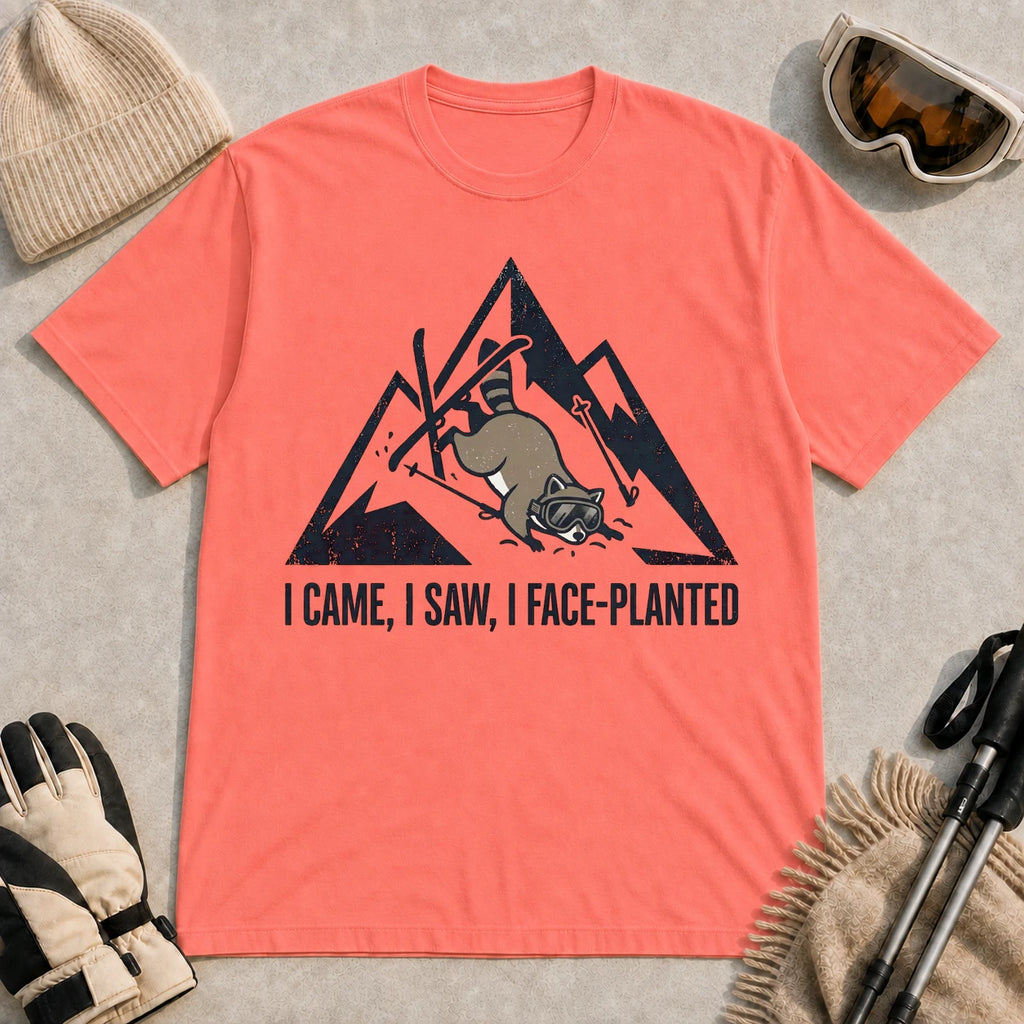 Coral Silk tee featuring a raccoon face-planting into the snow beneath a distressed mountain graphic with the phrase “I Came, I Saw, I Face-Planted.”