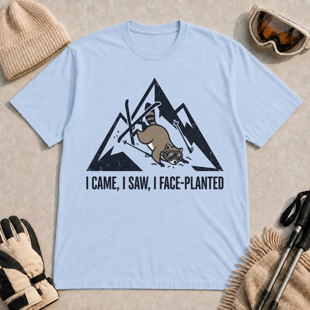 Light Blue tee featuring a raccoon face-planting into the snow beneath a distressed mountain graphic with the phrase “I Came, I Saw, I Face-Planted.”
