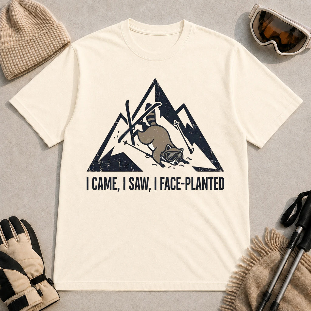 Natural tee featuring a raccoon face-planting into the snow beneath a distressed mountain graphic with the phrase “I Came, I Saw, I Face-Planted.”