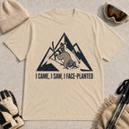 Sand tee featuring a raccoon face-planting into the snow beneath a distressed mountain graphic with the phrase “I Came, I Saw, I Face-Planted.”