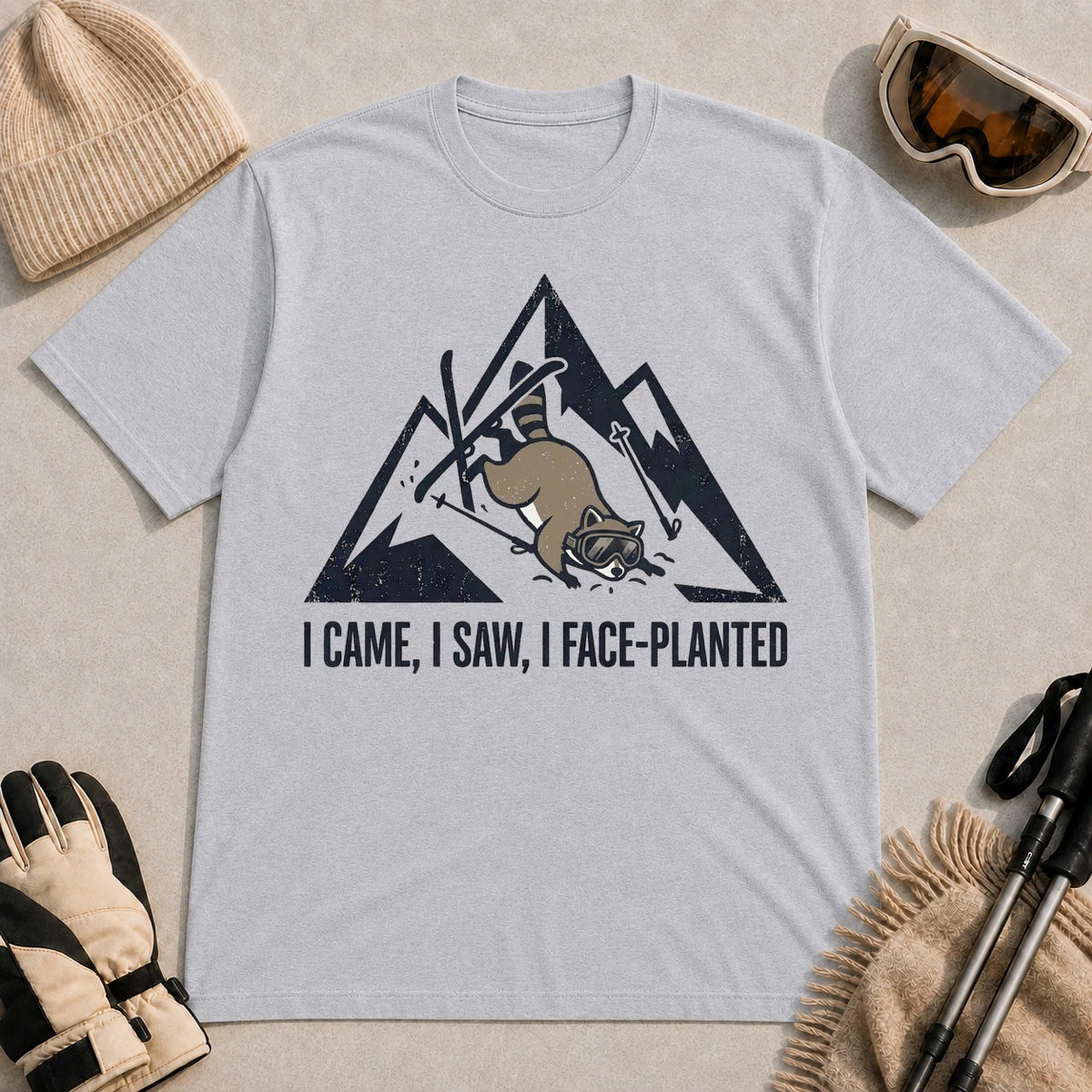 Sport Grey tee featuring a raccoon face-planting into the snow beneath a distressed mountain graphic with the phrase “I Came, I Saw, I Face-Planted.”