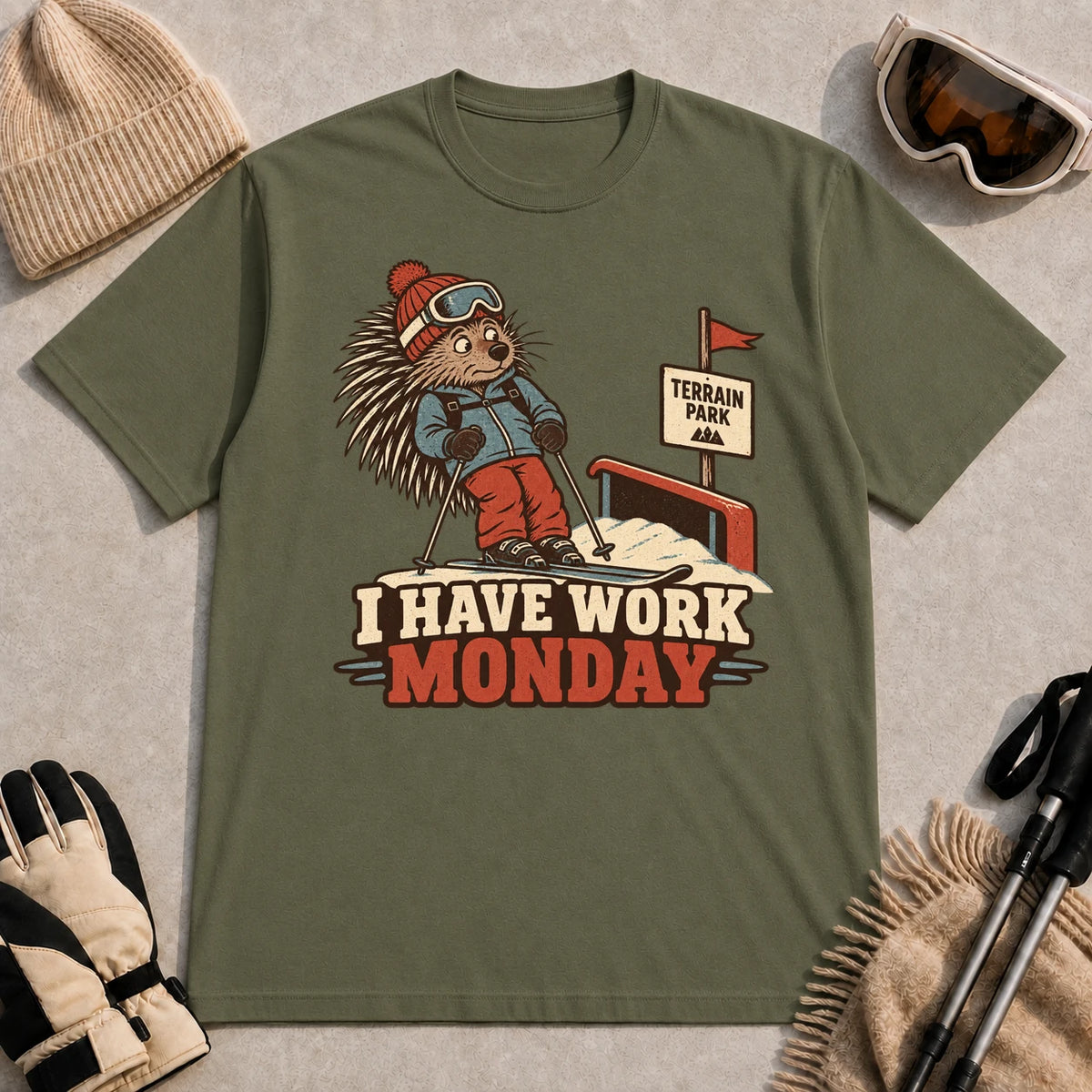 Military Green tee featuring a cautious porcupine skier beside a terrain park rail and sign above the phrase “I Have Work Monday.”