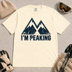 Ivory tee featuring a distressed navy double-mountain graphic above the phrase “I’m Peaking.”