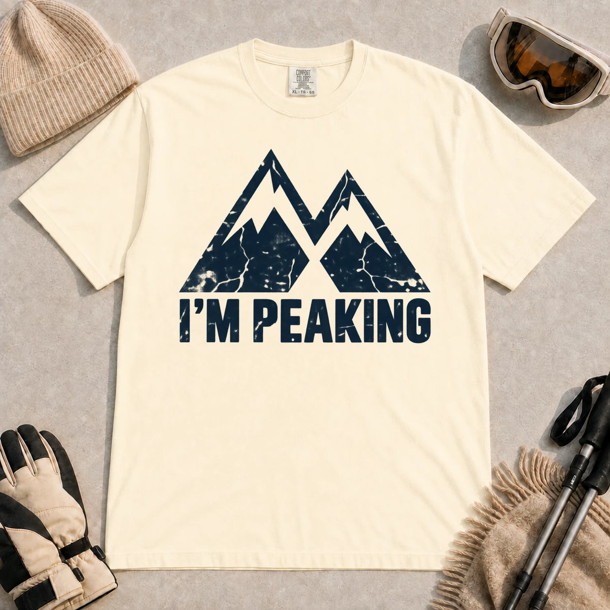 Ivory tee featuring a distressed navy double-mountain graphic above the phrase “I’m Peaking.”
