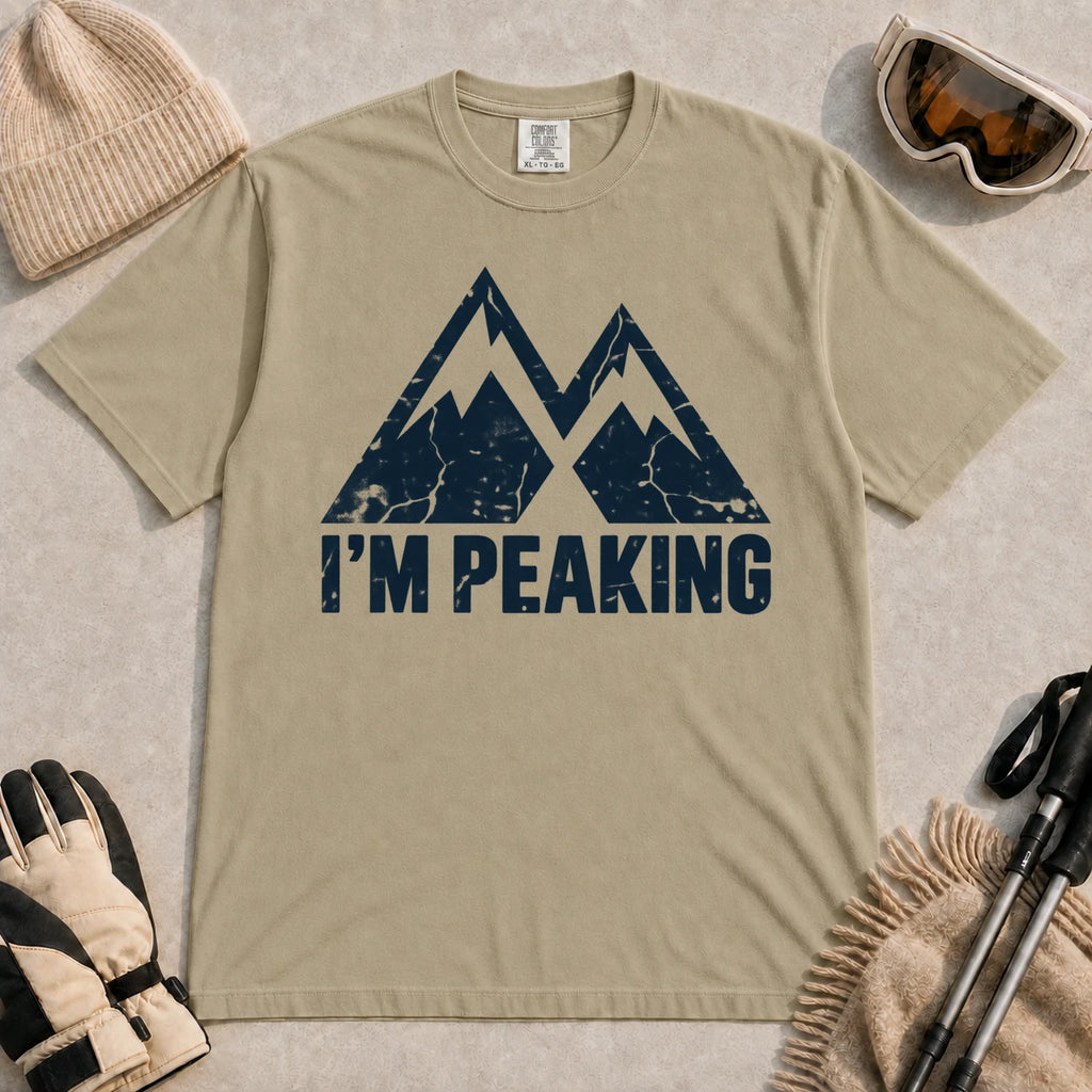 Khaki tee featuring a distressed navy double-mountain graphic above the phrase “I’m Peaking.”