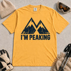 Mustard tee featuring a distressed navy double-mountain graphic above the phrase “I’m Peaking.”