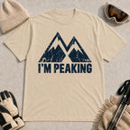 Sand tee featuring a distressed navy double-mountain graphic above the phrase “I’m Peaking.”