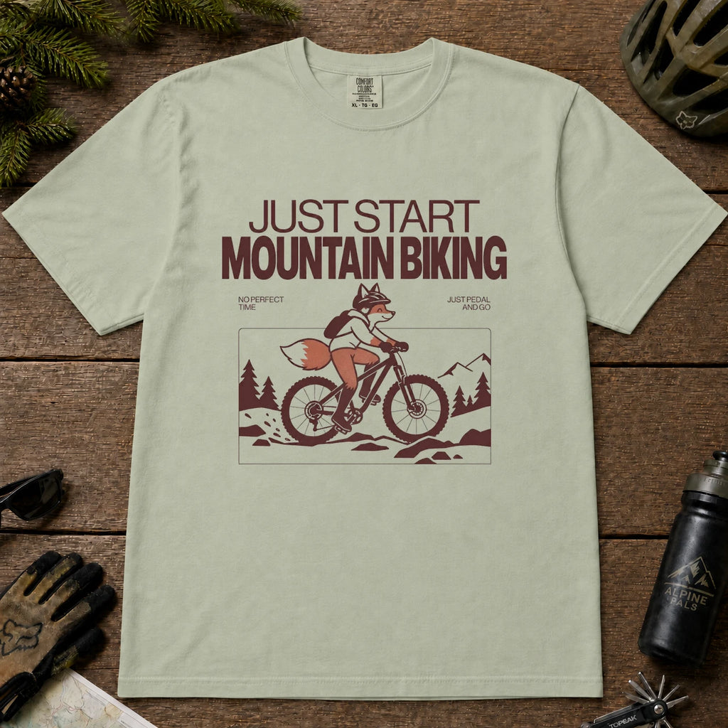 Bay tee featuring a fox mountain biking through a minimalist trail scene with the phrases “Just Start Mountain Biking,” “No Perfect Time,” and “Just Pedal and Go.”