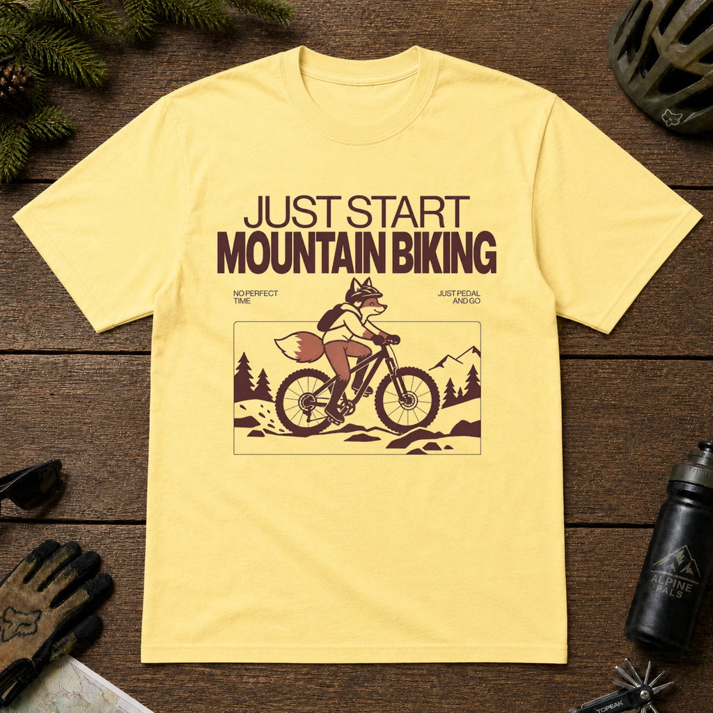 Cornsilk tee featuring a fox mountain biking through a minimalist trail scene with the phrases “Just Start Mountain Biking,” “No Perfect Time,” and “Just Pedal and Go.”