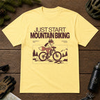 Cornsilk tee featuring a fox mountain biking through a minimalist trail scene with the phrases “Just Start Mountain Biking,” “No Perfect Time,” and “Just Pedal and Go.”