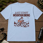 Light Blue tee featuring a fox mountain biking through a minimalist trail scene with the phrases “Just Start Mountain Biking,” “No Perfect Time,” and “Just Pedal and Go.”