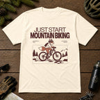 Natural tee featuring a fox mountain biking through a minimalist trail scene with the phrases “Just Start Mountain Biking,” “No Perfect Time,” and “Just Pedal and Go.”