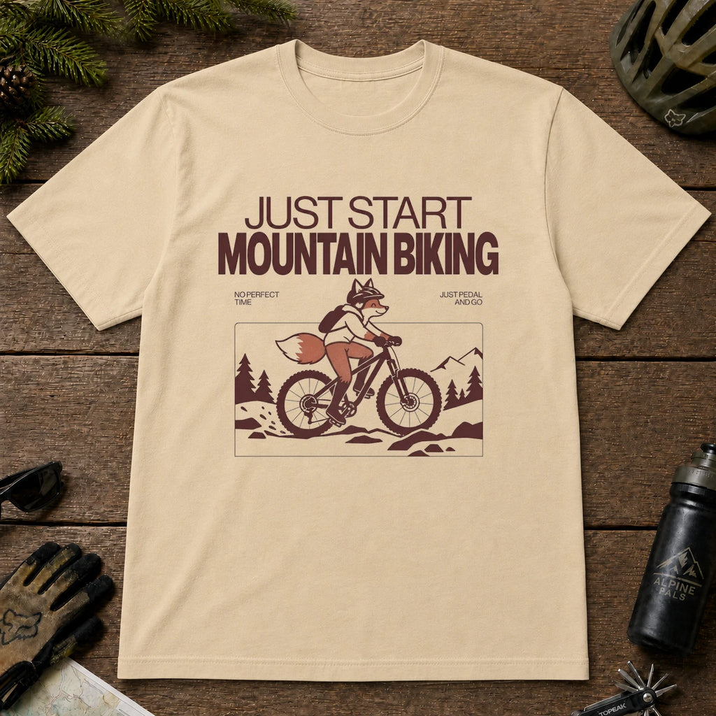 Sand tee featuring a fox mountain biking through a minimalist trail scene with the phrases “Just Start Mountain Biking,” “No Perfect Time,” and “Just Pedal and Go.”