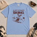 Washed Denim tee featuring a moose skiing through a minimalist mountain scene with the phrases “Just Start Skiing,” “No Perfect Time,” and “Just Click In and Go.”