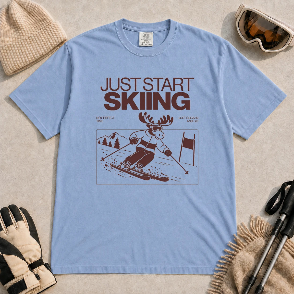 Washed Denim tee featuring a moose skiing through a minimalist mountain scene with the phrases “Just Start Skiing,” “No Perfect Time,” and “Just Click In and Go.”