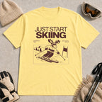 Cornsilk tee featuring a moose skiing through a minimalist mountain scene with the phrases “Just Start Skiing,” “No Perfect Time,” and “Just Click In and Go.”