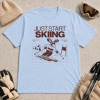 Washed Denim tee featuring a moose skiing through a minimalist mountain scene with the phrases “Just Start Skiing,” “No Perfect Time,” and “Just Click In and Go.”