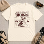 Natural tee featuring a moose skiing through a minimalist mountain scene with the phrases “Just Start Skiing,” “No Perfect Time,” and “Just Click In and Go.”