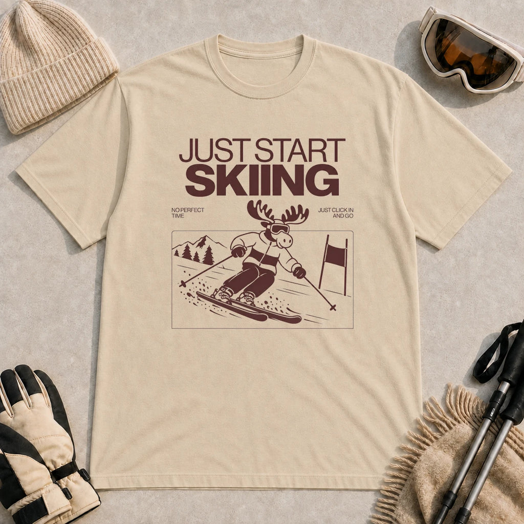 Sand tee featuring a moose skiing through a minimalist mountain scene with the phrases “Just Start Skiing,” “No Perfect Time,” and “Just Click In and Go.”